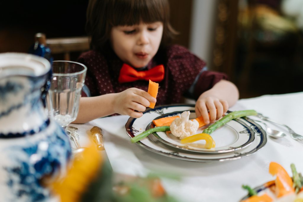 a little girl eating vegetables at the table